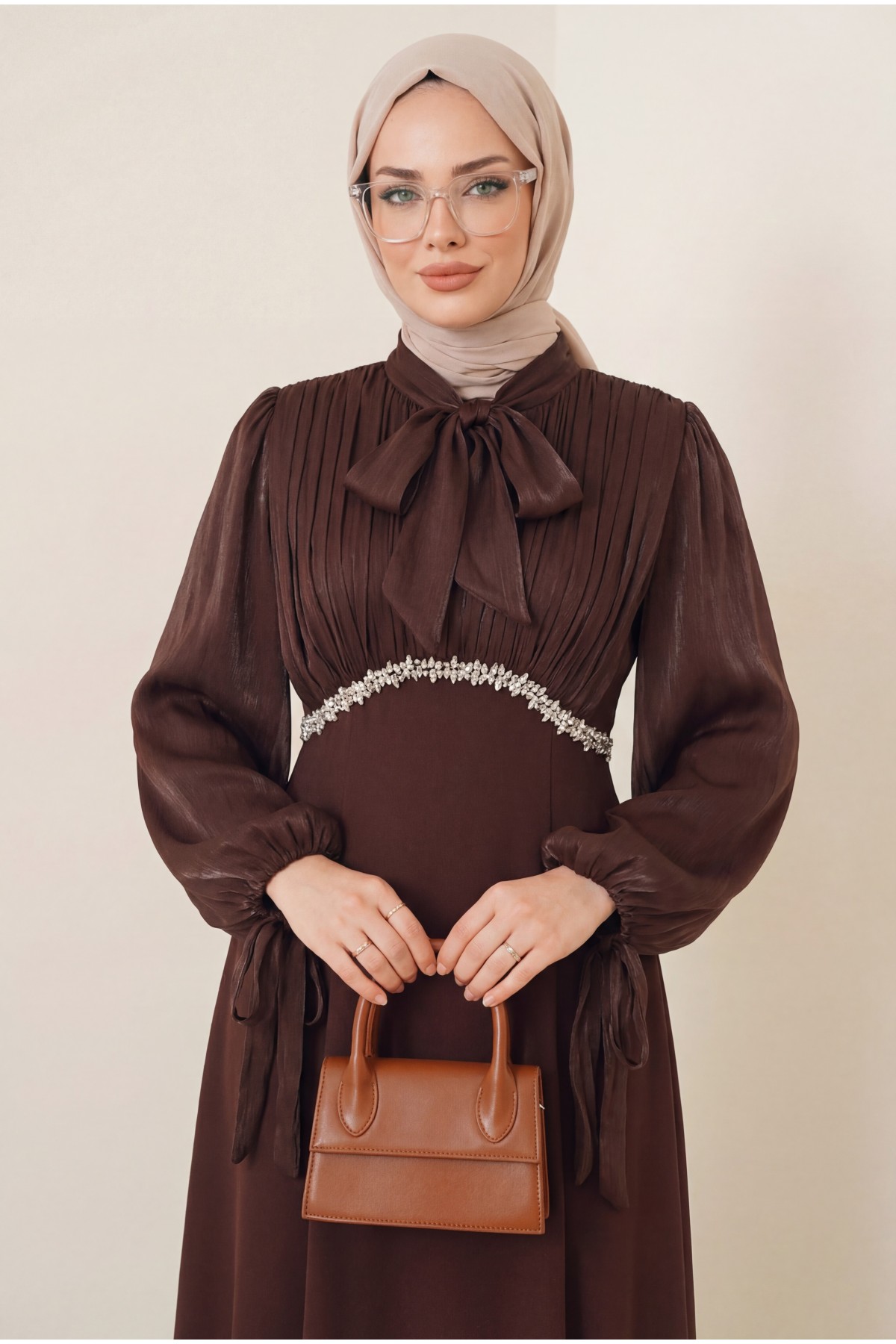 بلوزة مطوية بياقة وأكمام برباط، وتنورة من الكريب الساتان اللامع. -بنى